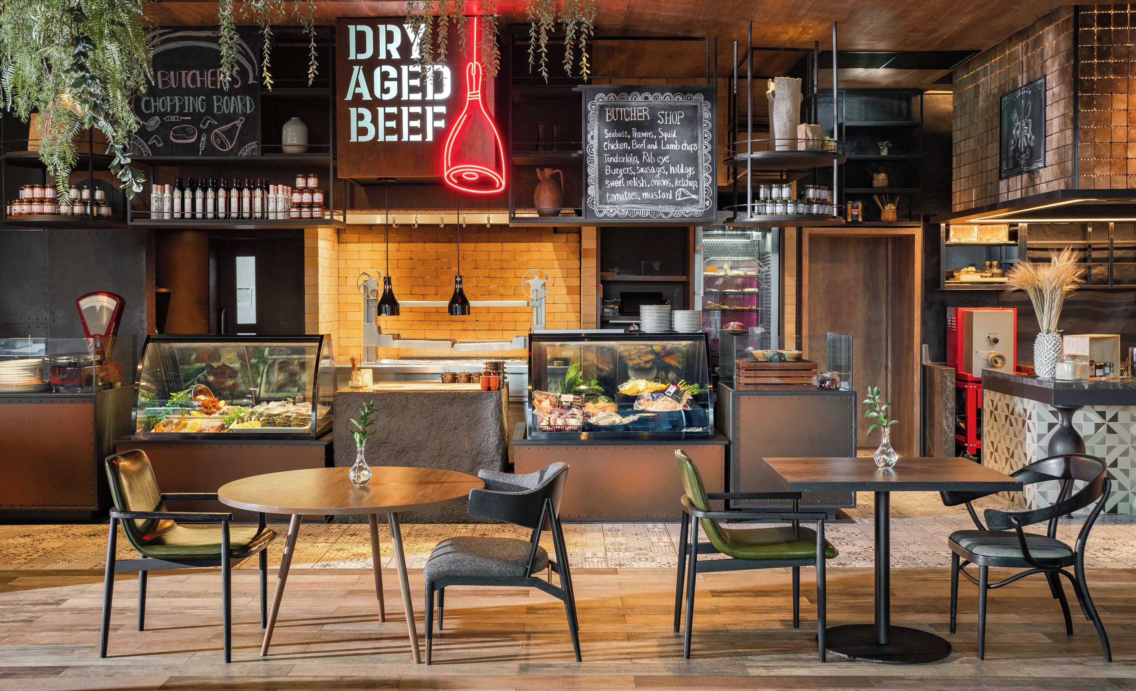 A restaurant interior with a chalkboard menu, a glass display case with food, and a seating area with tables and chairs.