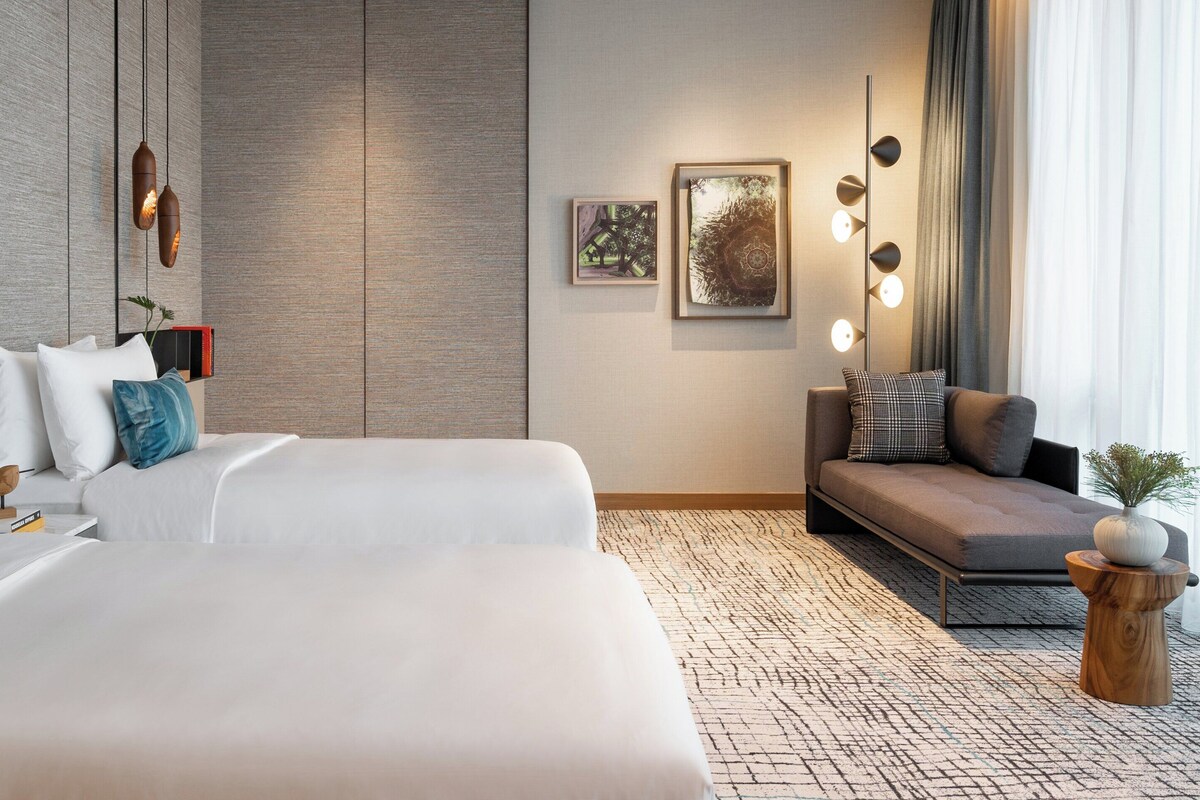 Une chambre d’hôtel moderne avec un grand lit, un canapé et une petite table sur laquelle est posé un vase.