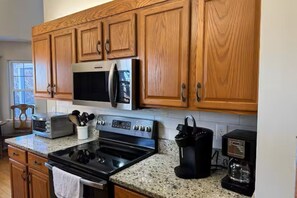 Una cocina con armarios de madera, microondas, horno, tostadora y cafetera.