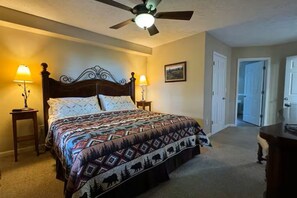 A bedroom with a bed, two bedside lamps, a ceiling fan, and a door.