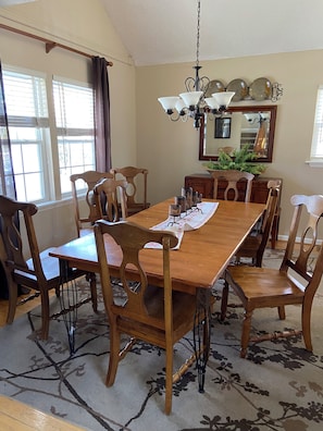 A dining room with a wooden table, chairs, a chandelier, and a mirror on the wall.