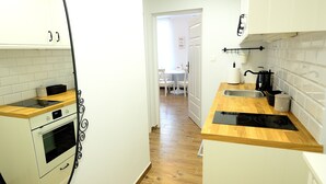 Cocina compacta con armarios blancos, encimera de madera, horno integrado y cocina de inducción negra.