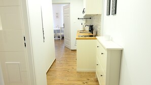 Un pasillo estrecho con piso de madera, paredes blancas y una zona de cocina con armarios blancos y una encimera.