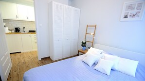 Un dormitorio con cama, almohadas, una mesita de noche, una escalera de madera y un armario blanco.