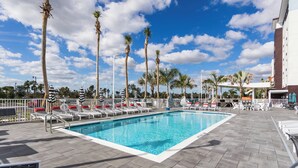 A swimming pool with lounge chairs and umbrellas, surrounded by palm trees and a clear sky. - TownePlace Suites by Marriott Port St. Lucie I-95 (Port Saint Lucie)