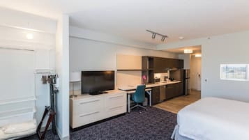 A hotel room with a bed, a desk with a computer, a chair, a TV, and a kitchenette.