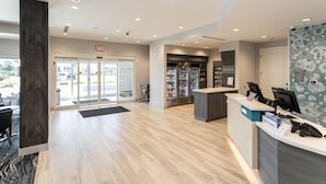 A hotel reception area with a wooden floor, a reception desk, a minibar, and a view of the outside through the glass doors. - TownePlace Suites by Marriott Port St. Lucie I-95 (Port Saint Lucie)