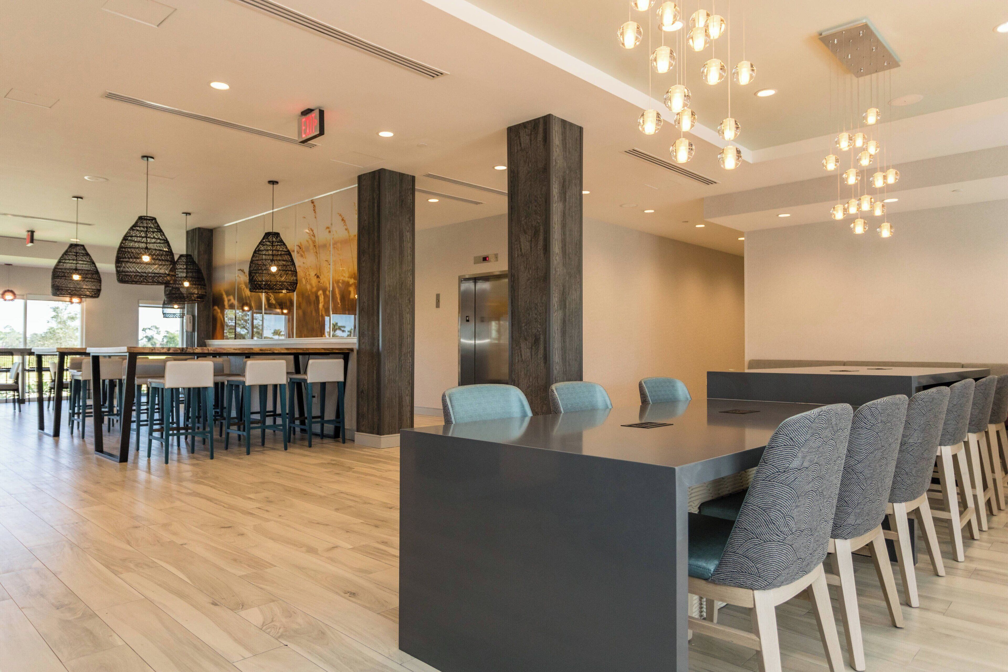 A modern dining area with a long table, chairs, and hanging pendant lights.