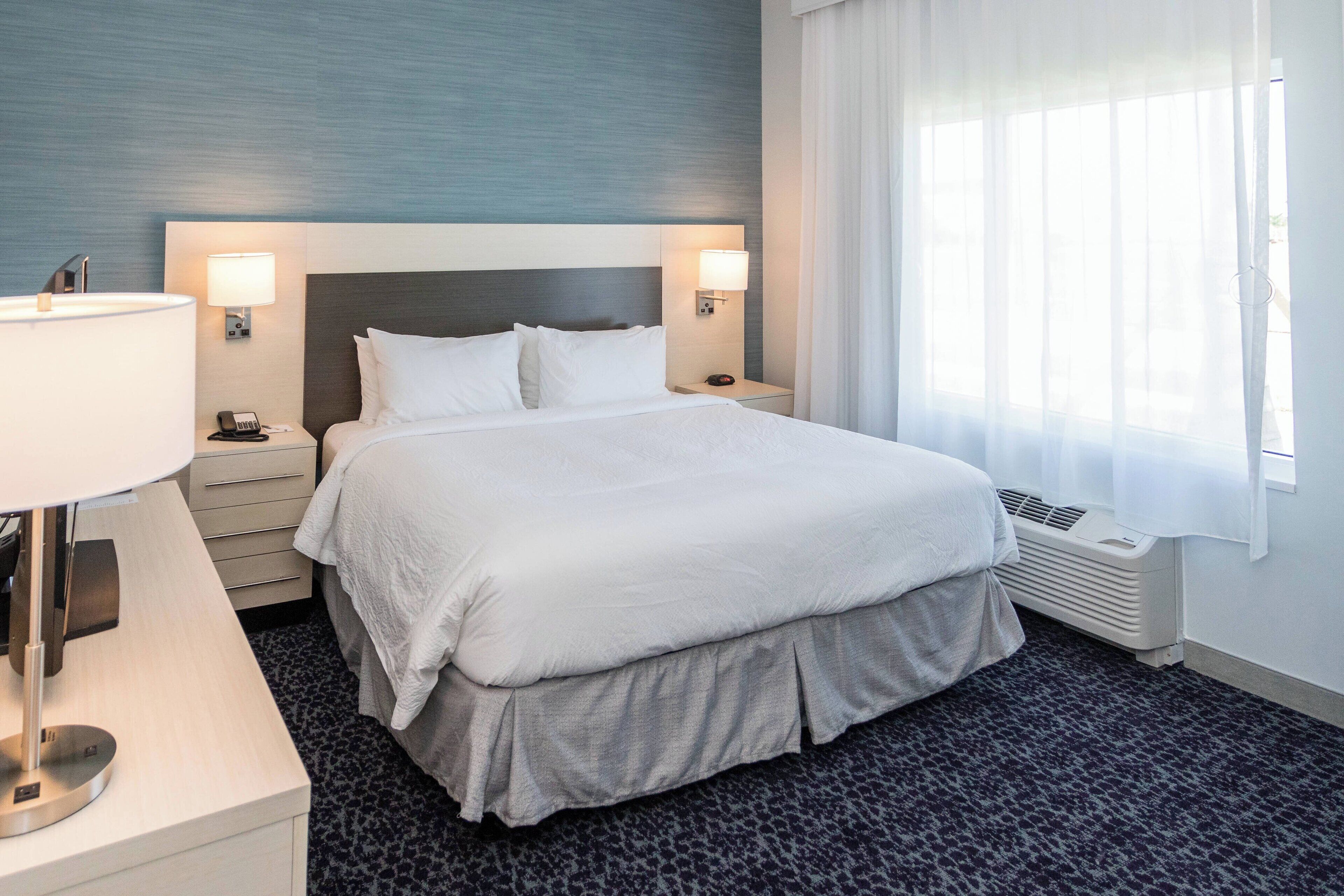 Habitación de hotel con una cama grande, dos lámparas de noche, un escritorio con lámpara y una ventana con cortinas translúcidas.