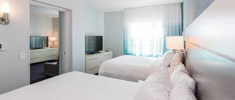 Une chambre d’hôtel avec deux lits, une télévision, un bureau et une salle de bain visible à travers une porte ouverte.