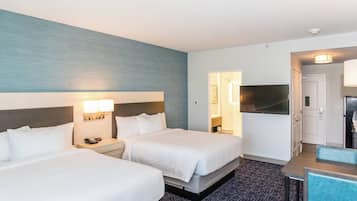 Een hotelkamer met twee bedden, een bureau, een televisie en een kitchenette.