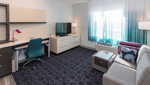 A hotel room with a desk, chair, TV, air conditioning unit, and a sofa. - TownePlace Suites by Marriott Port St. Lucie I-95 (Port Saint Lucie)