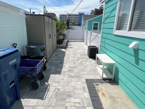 A narrow pathway between two buildings with a trash bin and a blue cart. - Ocean Breeze - Cozy Beach Cottage across from the beach. Pet friendly! (Madeira Beach)