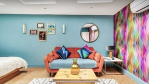 Une pièce avec un mur bleu, un canapé avec des coussins, un miroir rond et un motif géométrique coloré sur le mur.