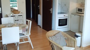 Una cucina compatta con forno a microonde, forno e pensili bianchi. È presente un'area pranzo con un tavolo apparecchiato per due e una sedia in vimini.