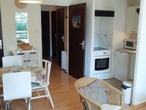 Una cucina compatta con forno a microonde, forno e pensili bianchi. È presente un'area pranzo con un tavolo apparecchiato per due e una sedia in vimini.