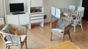 Un soggiorno moderno con televisione, poltrone in vimini, un tavolo da pranzo apparecchiato per quattro persone e opere d'arte alle pareti.