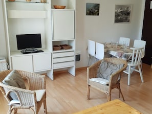 Un soggiorno moderno con televisione, poltrone in vimini, un tavolo da pranzo apparecchiato per quattro persone e opere d'arte alle pareti.