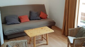 Un soggiorno con un divano grigio, un tavolino in legno, poltrone in vimini e un quadro floreale appeso alla parete.