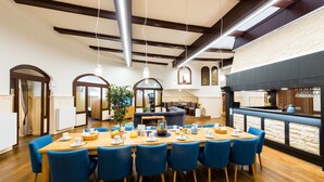 A spacious dining area with a long wooden table, blue chairs, and a modern kitchen in the background. - Vacation in the Harz Mountains the special *****Holiday apartments Burgkaiser im Zwinger Goslar (Goslar)