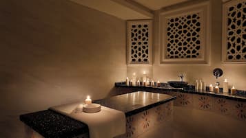 Un baño con lavamanos de mármol, varias velas y celosías decorativas en la ventana.