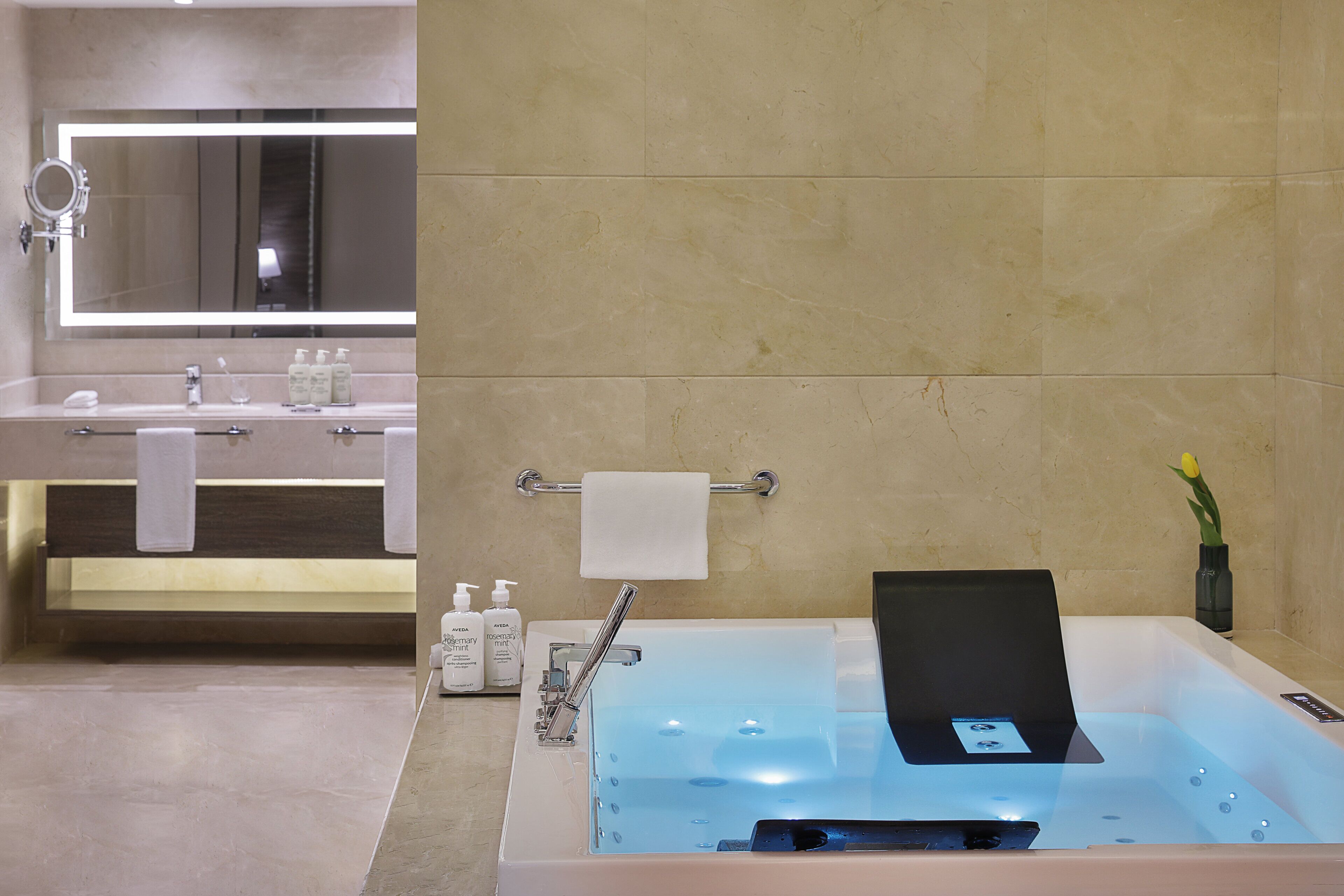 A modern bathroom with a large mirror, a sink with toiletries, and a bathtub with a laptop.