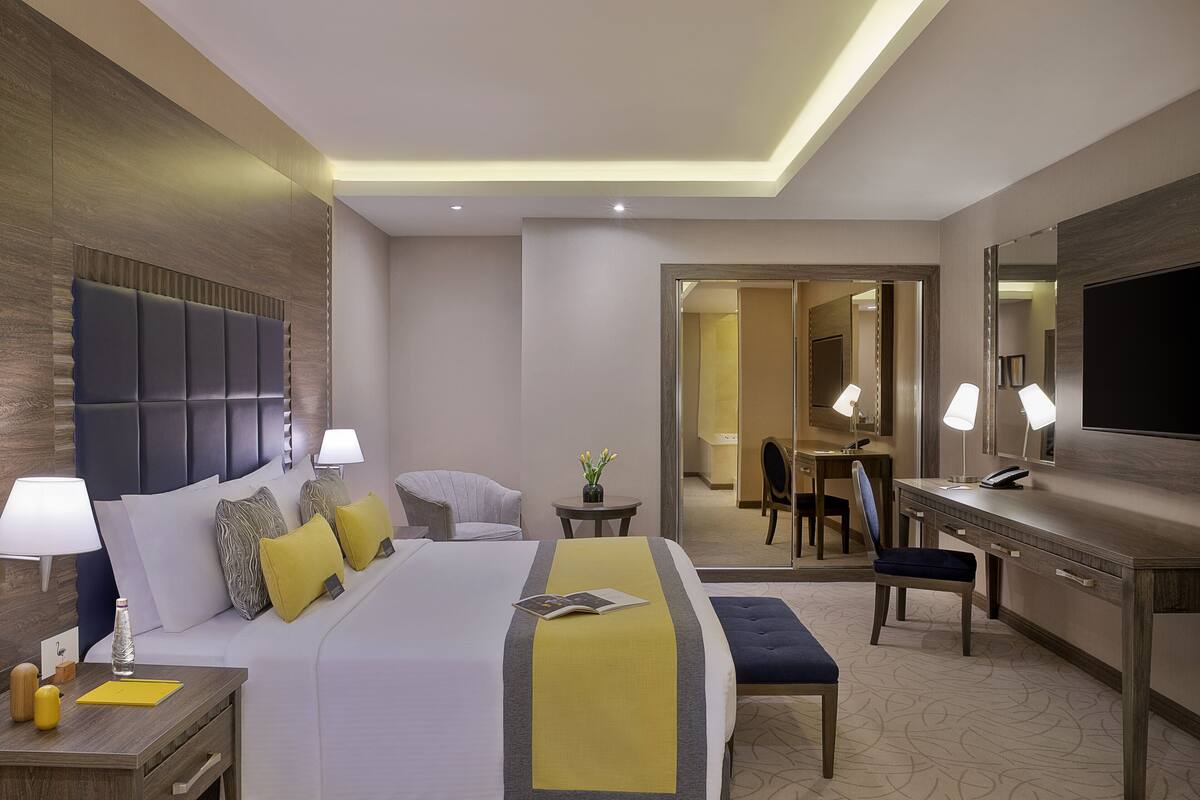 A hotel room with a large bed, bedside tables, a desk, and a TV.