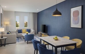 A modern living room with a sofa, chairs, a dining table, and a TV. - voco Al Khobar by IHG (Al Khobar)