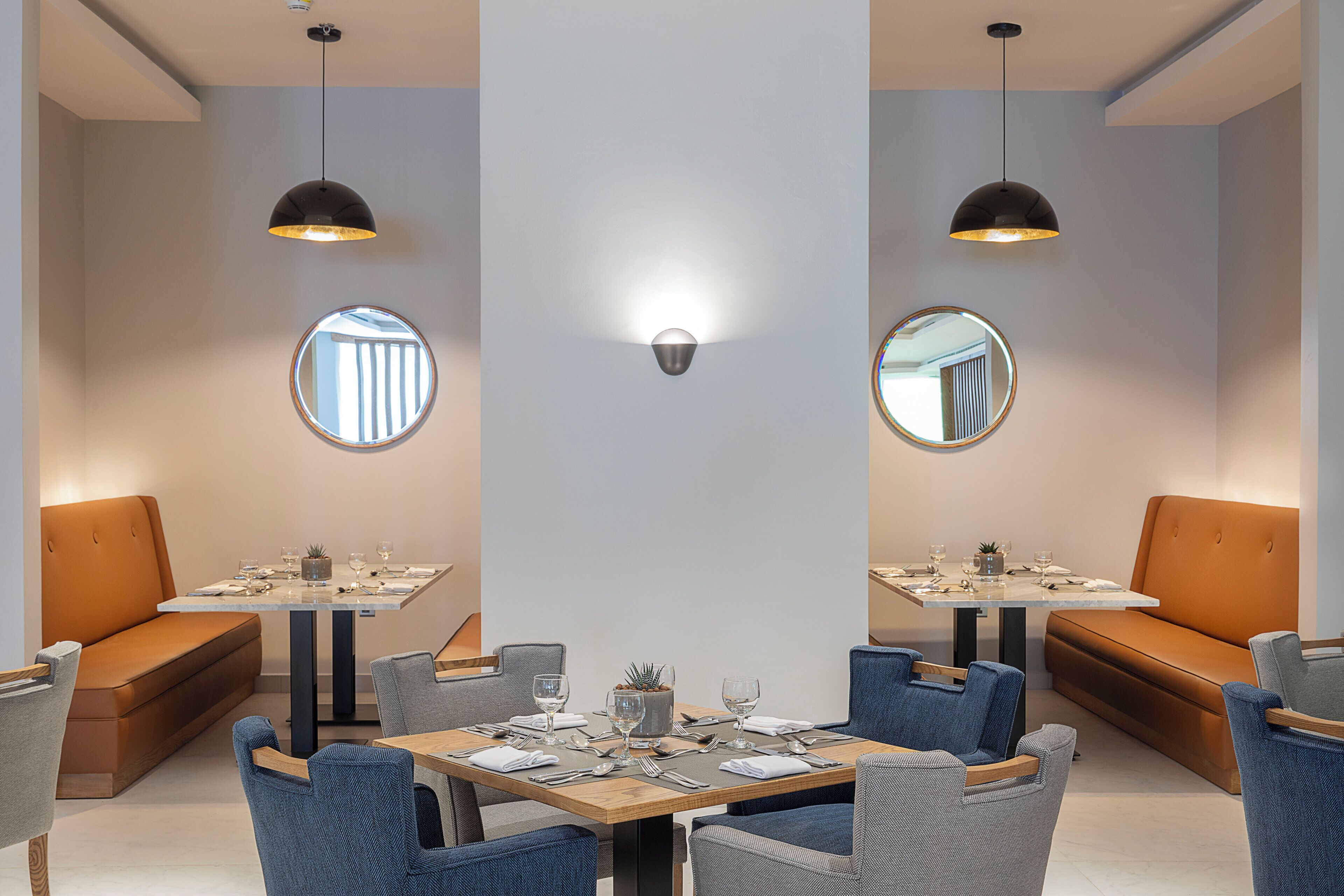 A modern dining area with round tables, blue upholstered chairs, and wall-mounted mirrors.