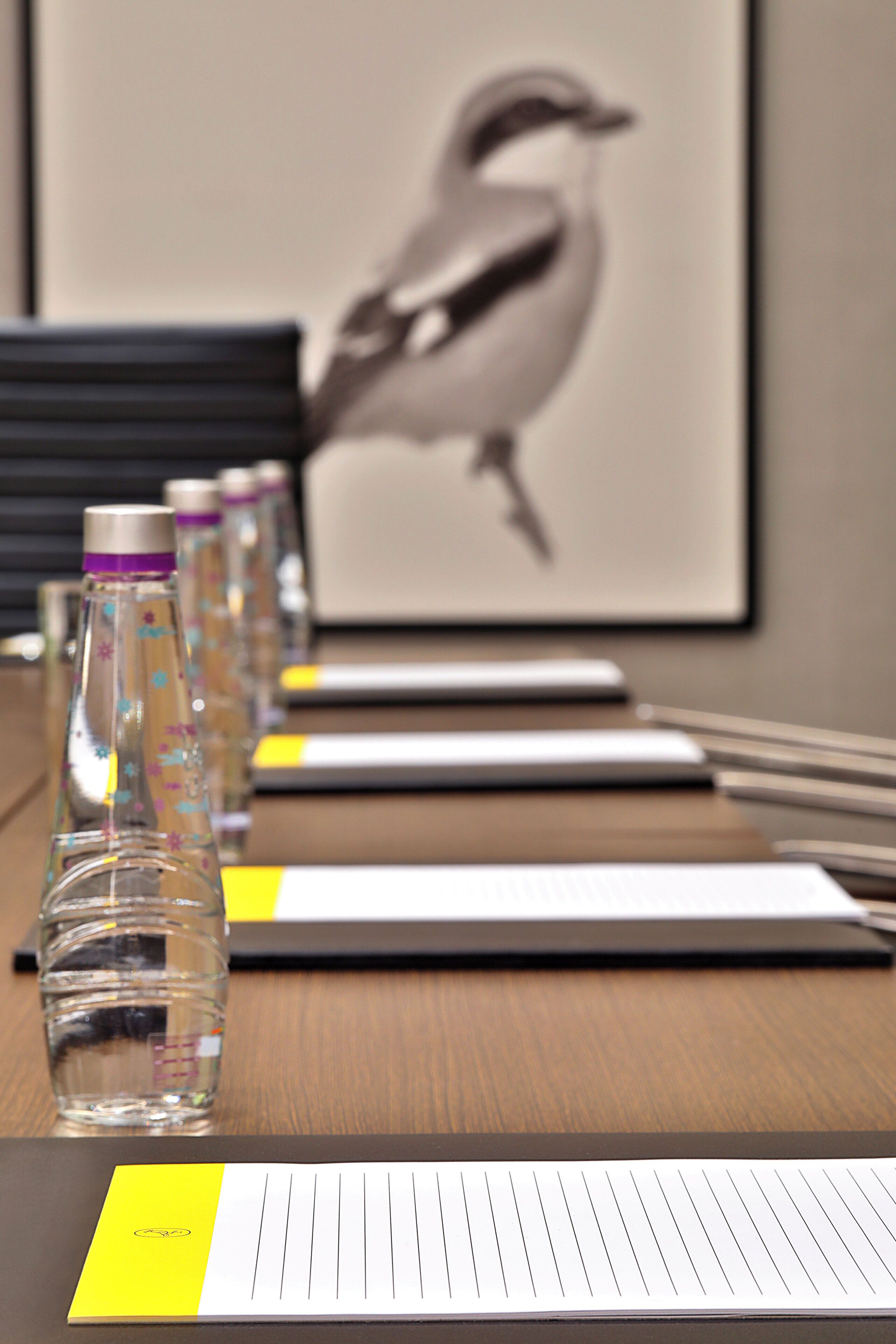 Een vergadertafel met een laptop, een notitieboekje en een pen. Twee waterflesjes en een gele post-it noot liggen op tafel.