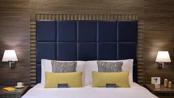 A hotel room with a large bed, two bedside tables, a nightstand, a wall-mounted lamp, and a framed picture on the nightstand.