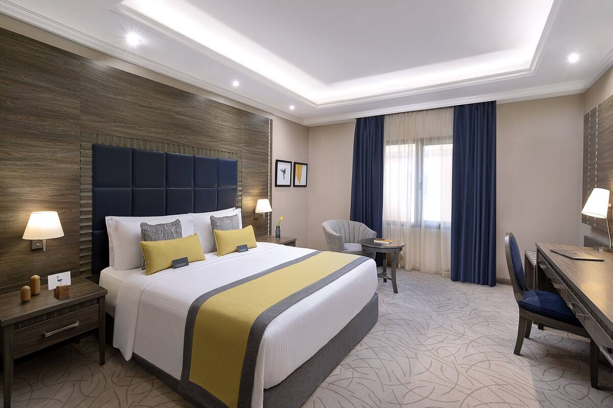 A hotel room with a large bed, bedside lamps, a desk, and a chair.