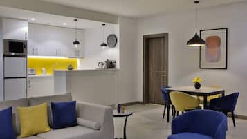Una sala moderna con un sofá gris, sillas azules y amarillas, una mesita y una zona de comedor con una mesa y sillas amarillas.