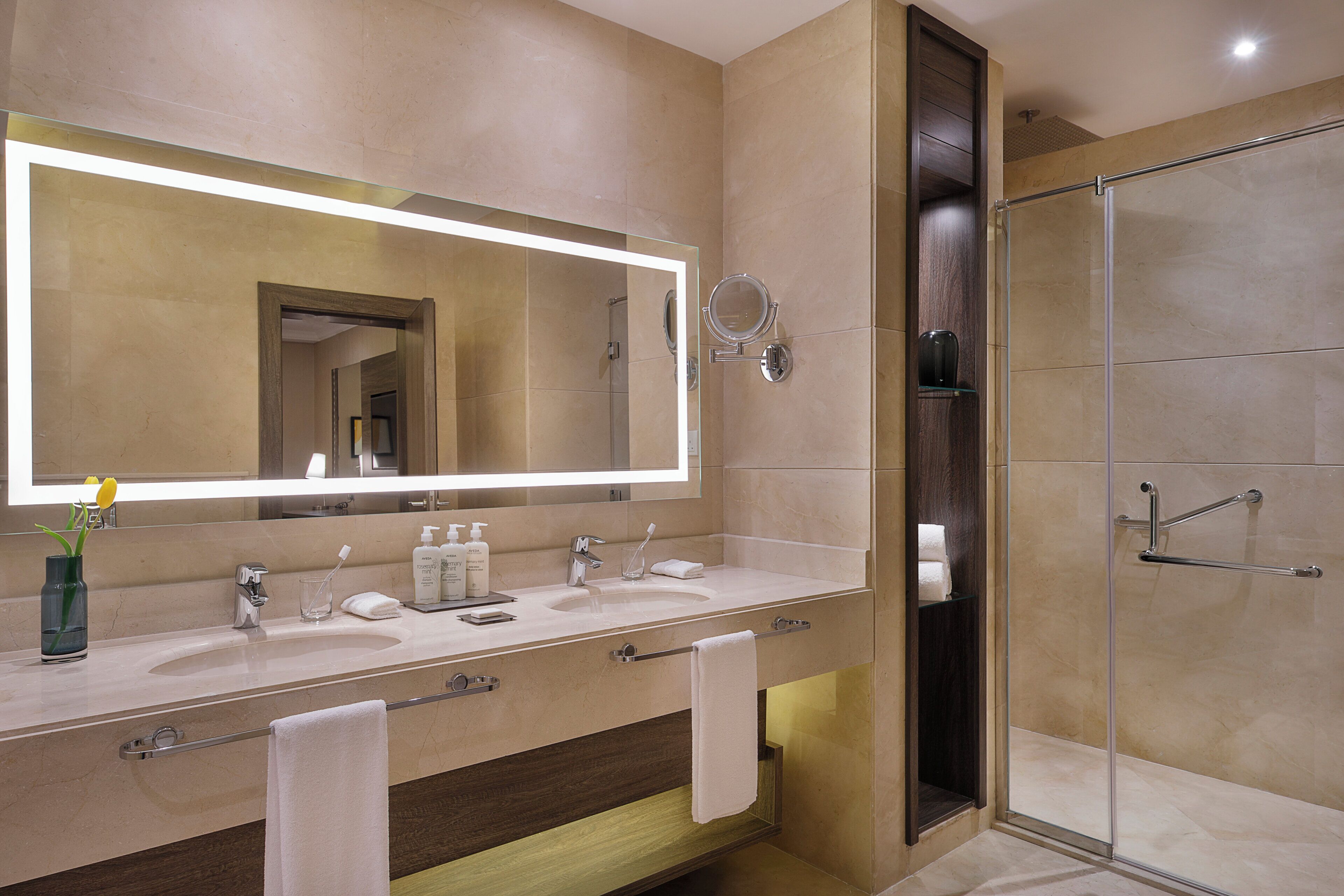 Un baño moderno con un espejo grande, lavamanos dobles, cabina de ducha de vidrio y un perchero para toallas.