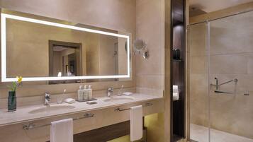 A modern bathroom with a large mirror, dual sinks, a glass shower enclosure, and a towel rack.
