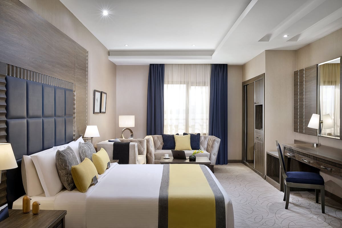 A hotel room with a large bed, a desk, a chair, a sofa, and a TV.
