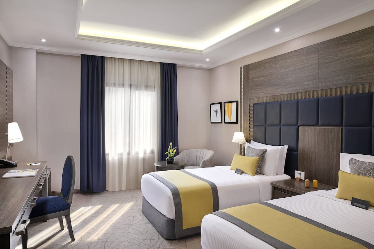 A hotel room with two beds, a desk, and a chair.