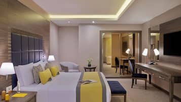 Habitación de hotel con cama, mesitas de noche, escritorio, silla, televisor y baño visible a través de una puerta abierta.