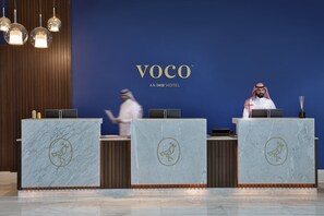 Welcome to VOCO, where guests are greeted by three elegant reception desks featuring a distinctive bird emblem.