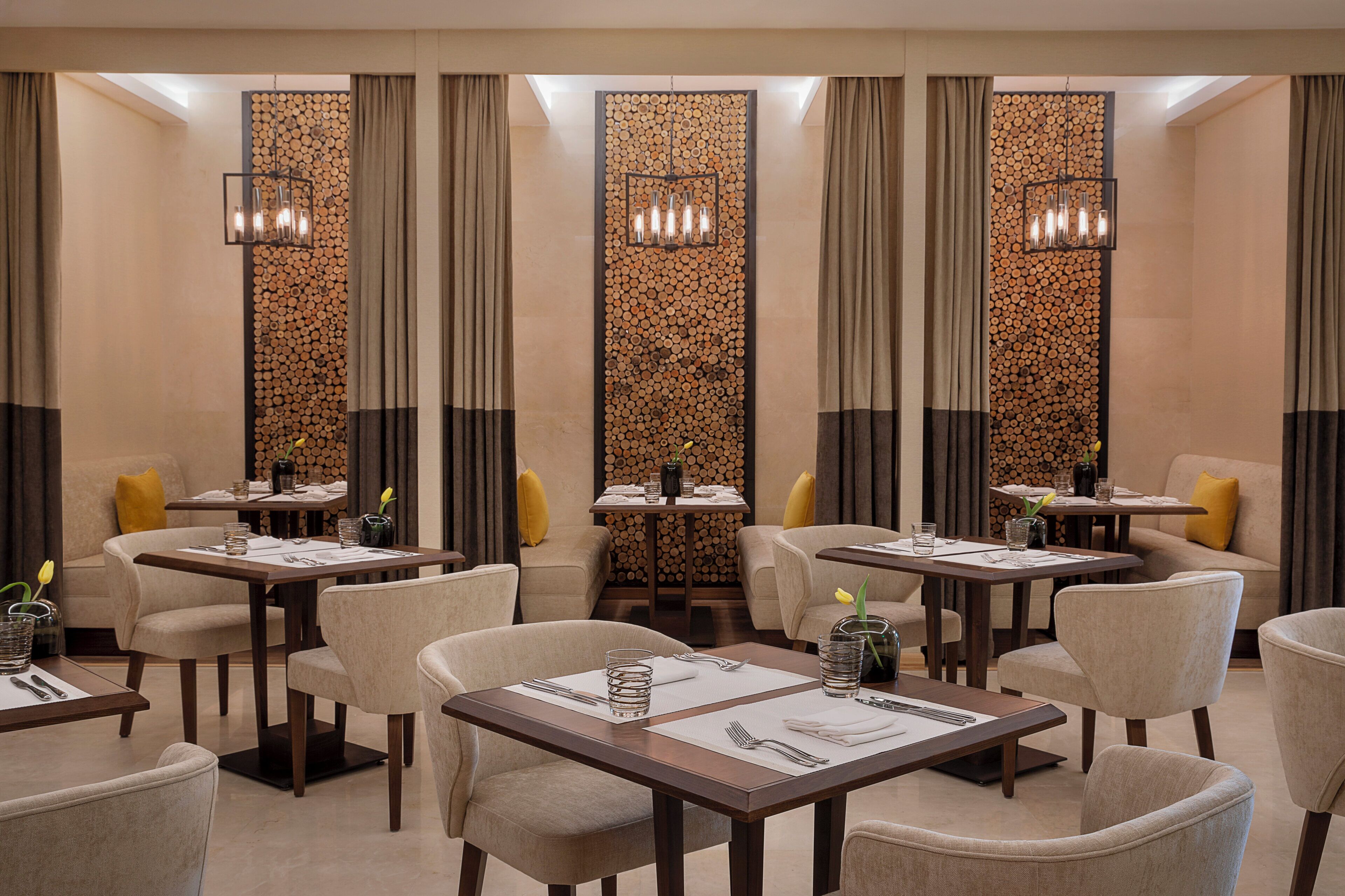 A hotel dining area with multiple tables, chairs, and a decorative wall with logs.