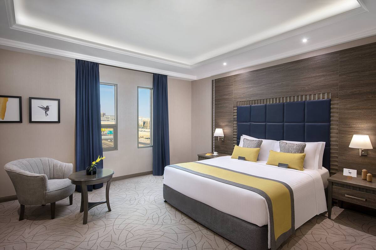 A modern hotel room with a large bed, a seating area, and a view of the city.