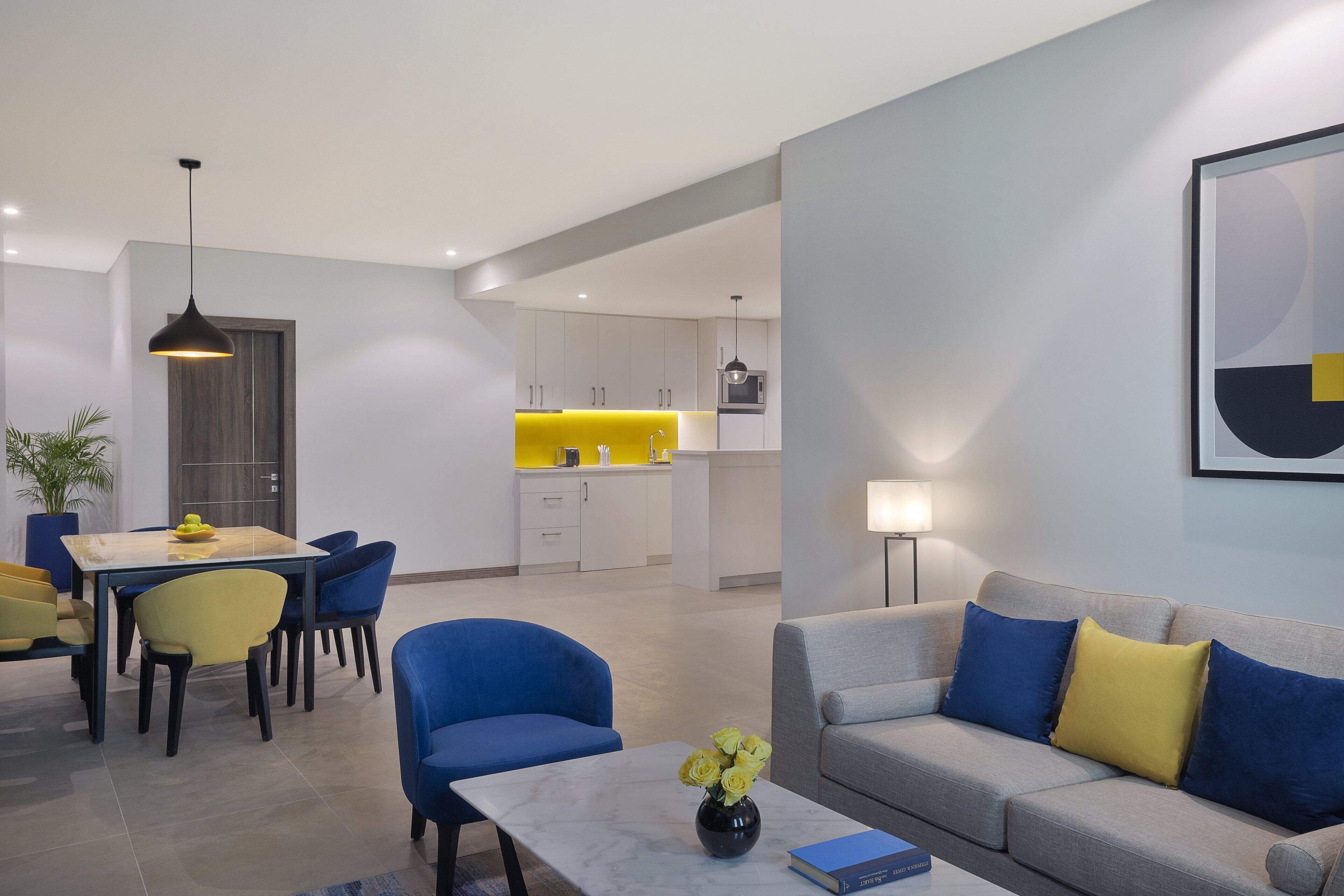 Ein modernes Wohnzimmer mit einem grauen Sofa, blauen Sesseln und einem Essbereich mit einem gelben Tisch und Stühlen.