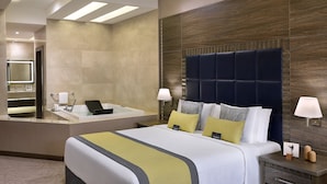 A hotel room with a large bed, a built-in bathtub, a vanity with a mirror, and two bedside lamps.
