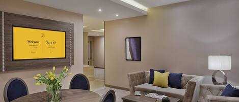A modern hotel room with a dining area, a sofa set, and a TV displaying a language selection screen.