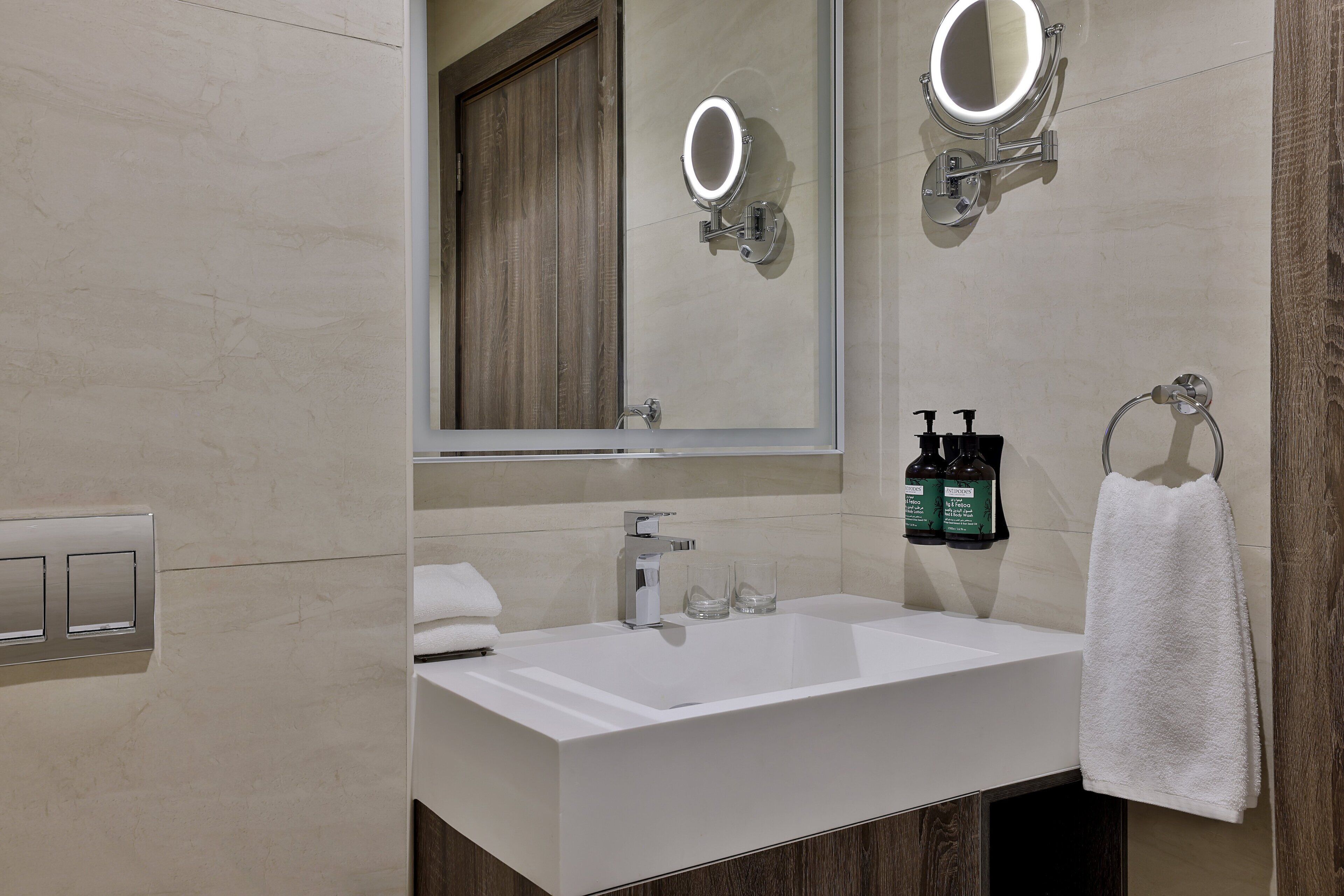 A modern bathroom with a large mirror, a white sink, and two bottles of shampoo.