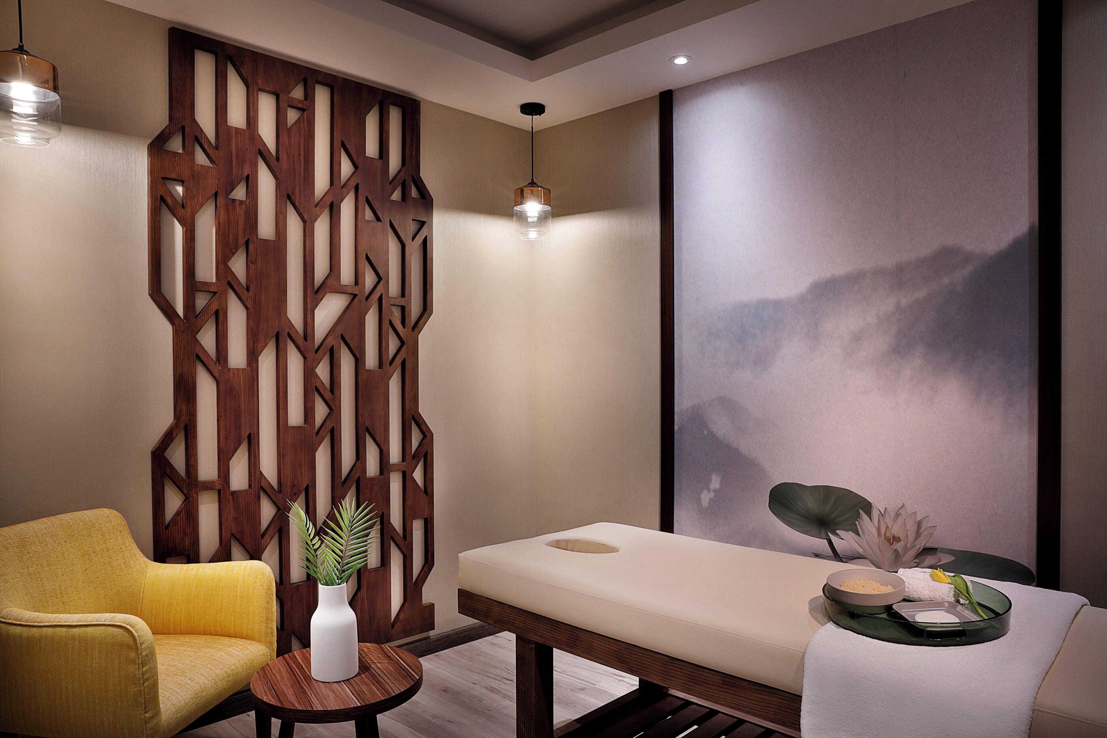 Ein Spa-Raum mit Massagetisch, einem gelben Sessel, einer Holzdekoration und einer Wandleuchte für Massagen.