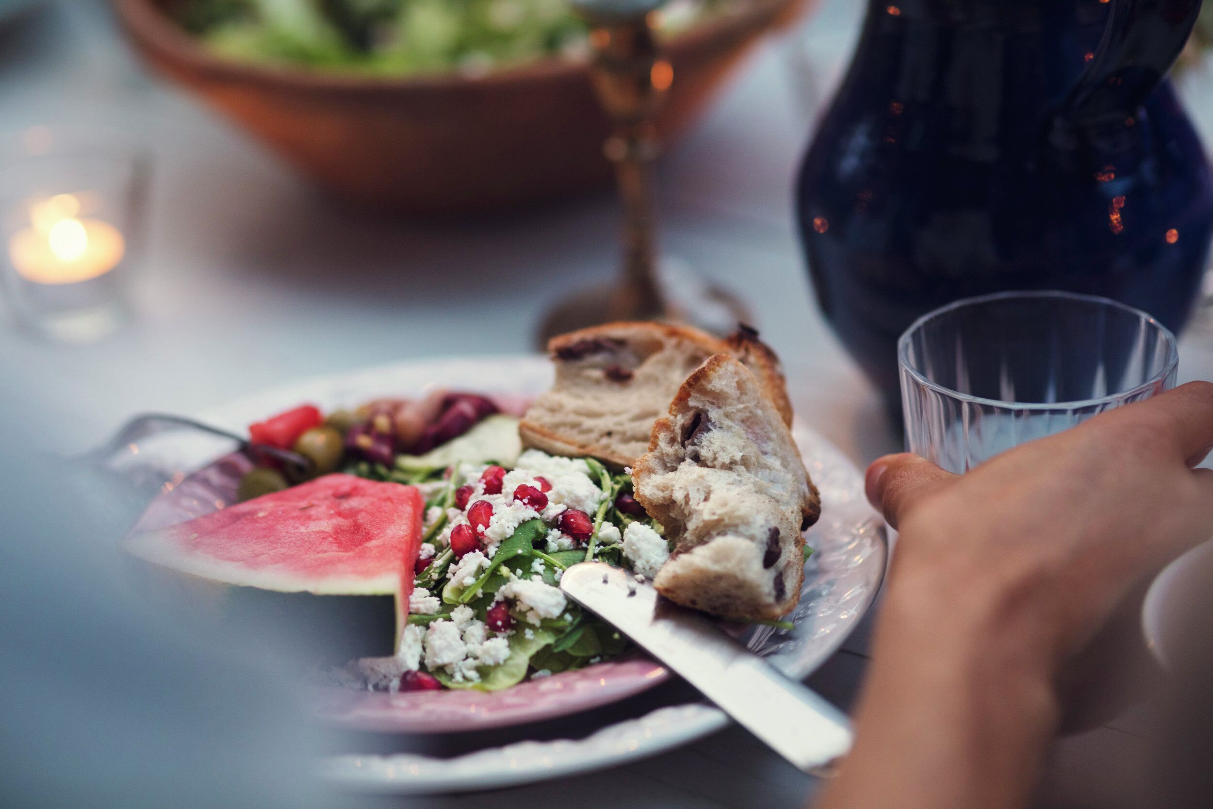 Une table à manger avec une assiette de nourriture, un verre et la main d’une personne.