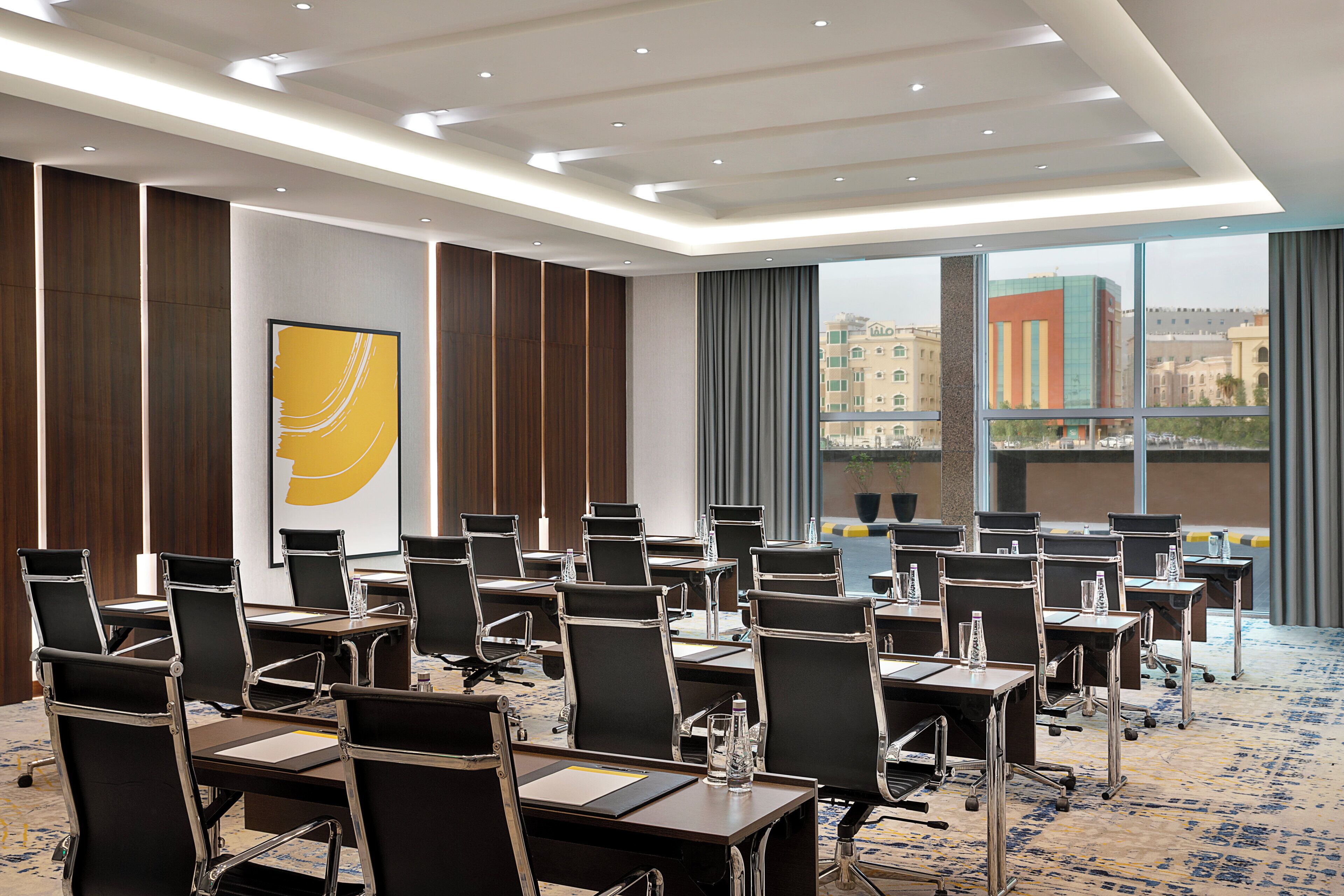Une salle de conférence dotée de plusieurs tables et chaises, de grandes fenêtres offrant une vue sur la ville et d’un aménagement intérieur moderne.