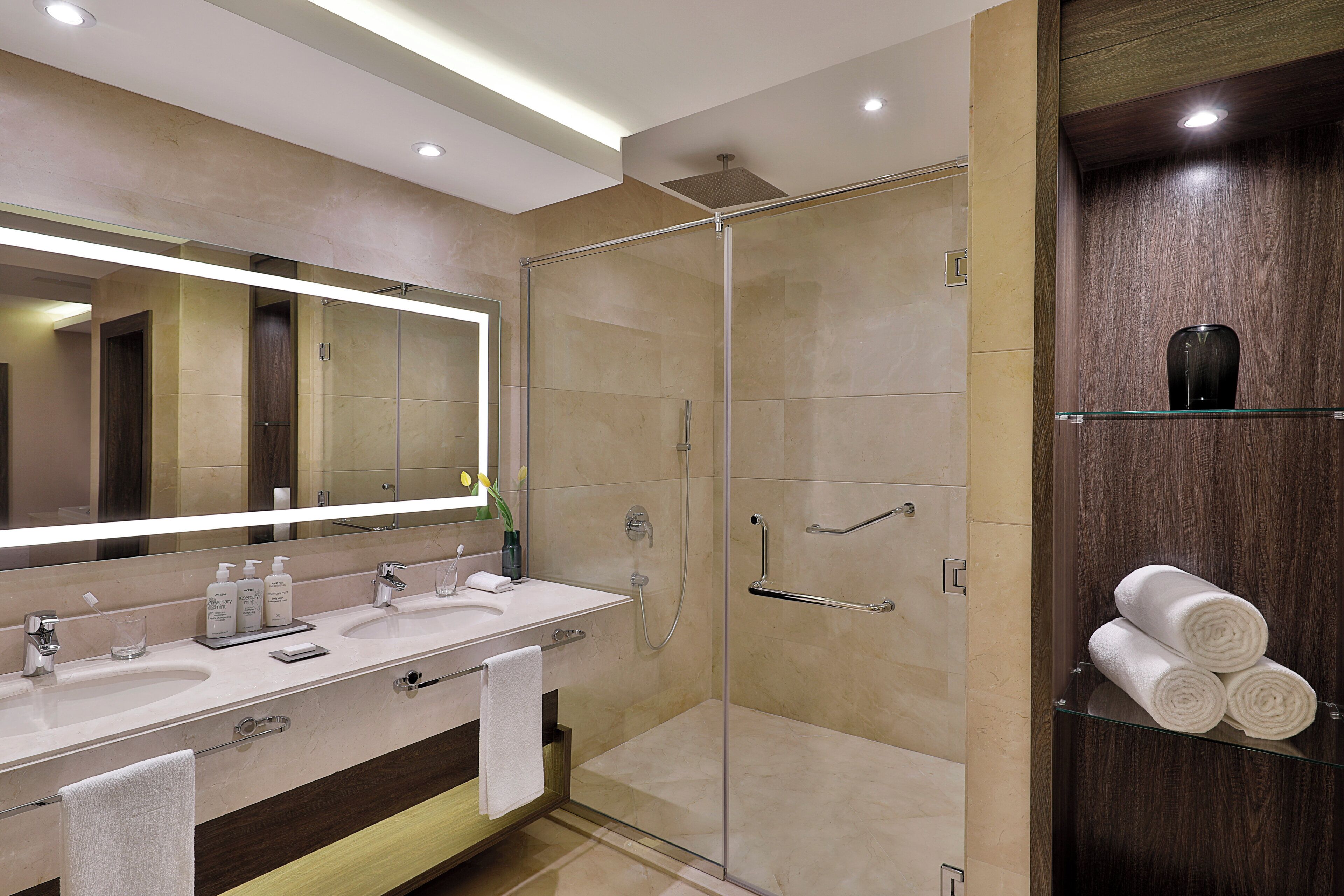 A modern bathroom with a glass-enclosed shower, a vanity with a mirror, and a glass shelf with towels.