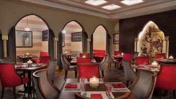 A restaurant with multiple dining tables, red upholstered chairs, and a decorative wall with a mural.